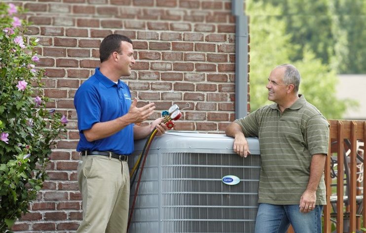 Technician consulting with homeowner about his HVAC while standing beside HVAC unit outside a brick home.