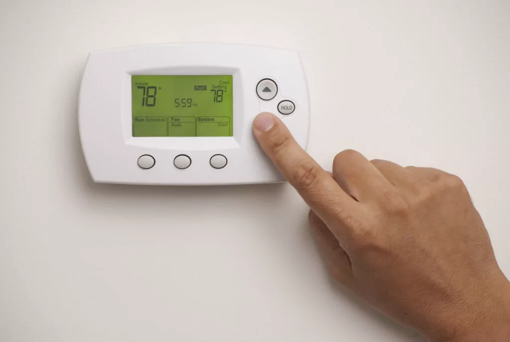 Thermostat on a white wall, with a hand adjusting the temperature.